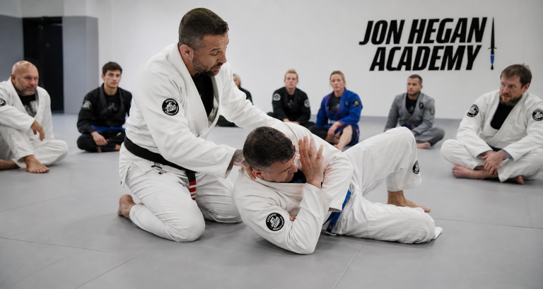 BJJ instructor demonstrating a fundamental ground escape to an adult beginner at Jon Hegan Academy.